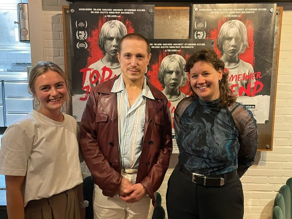 Zwei Frauen und ein Mann vor Filmplakaten des Filmes "Tod meiner Jugend"