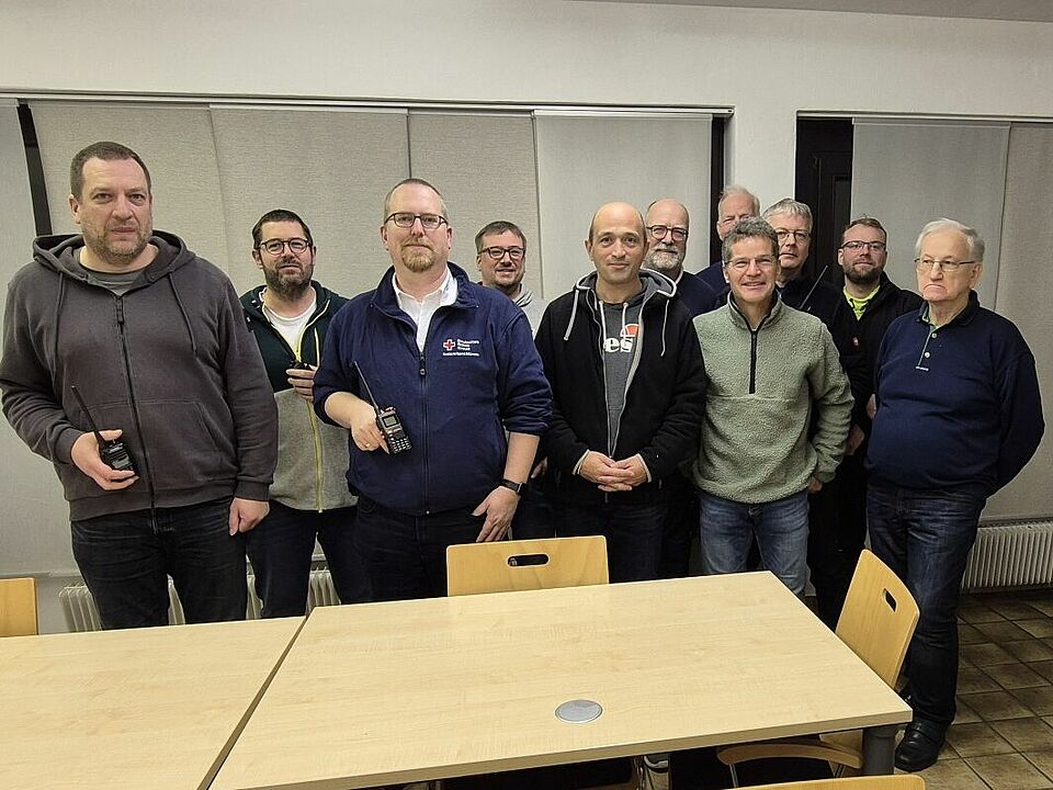 Gruppenbild mit elf Personen vor einem Holztisch. Einige Personen halten Funkgeräte in der Hand.