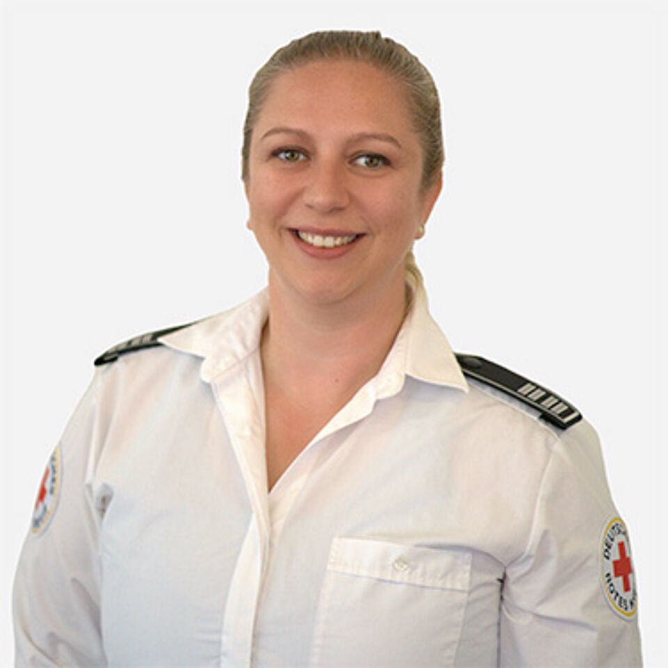 Frau mit blonden Haaren, weißem Hemd mit DRK-Logo und Schulterklappen vor weißem Hintergrund