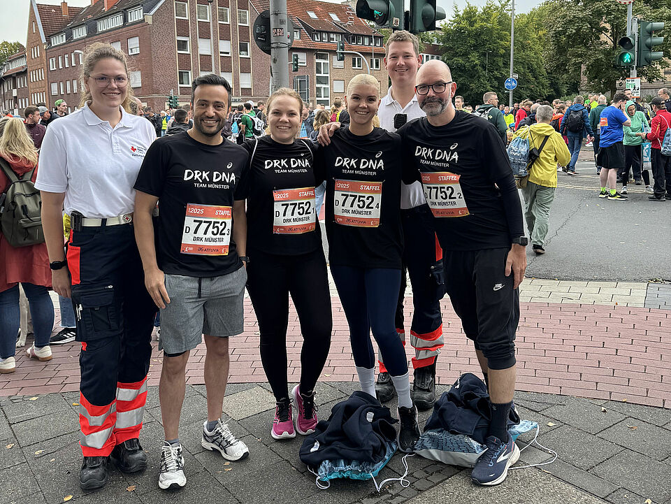 Gruppenfoto von vier Personen in schwarzen Laufshirts mit DRK-Aufdruck und zwei Personen in Einsatzkleidung