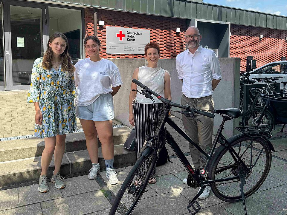 Siegerinnenehrung Vier Personen mit einem Fahrrad vor einem Gebäude mit DRK-Logo