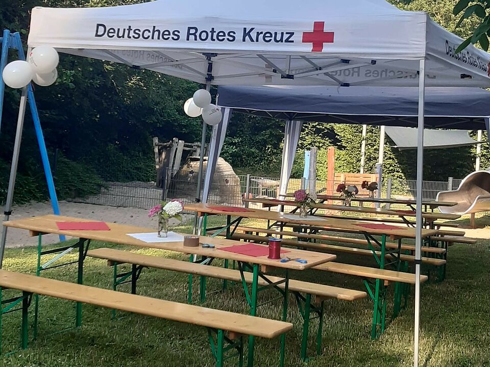 Ein weißer DRK-Pavillon, unter dem mehrere Bierzeltgarnituren stehen. Im Hintergrund ist ein Spielplatz zu sehen.