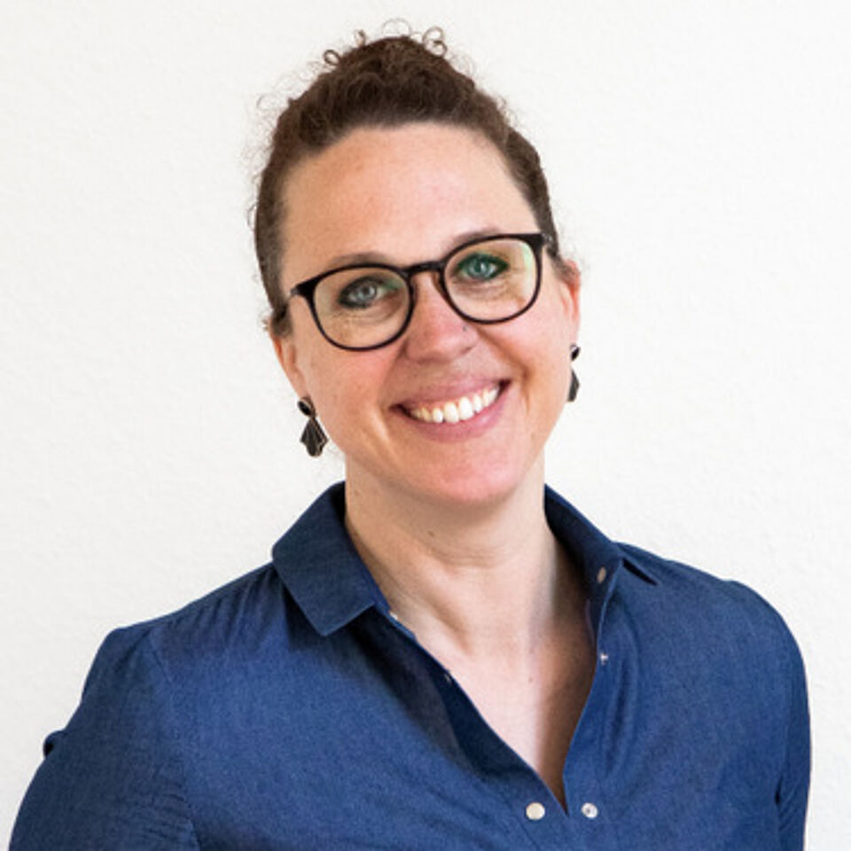 Frau mit braunen Haaren und blauer Bluse vor weißem Hintergrund