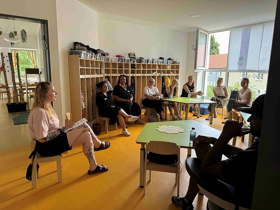 Neun Personen sitzen ine einem Stuhlkreis in der Garderobe einer Kita