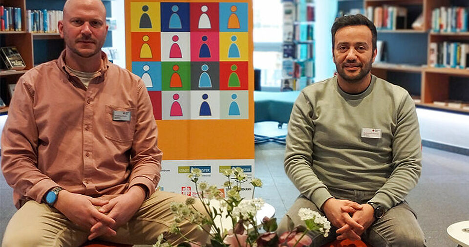 Wochen gegen Rassismus Zwei Personen sitzen vor dem Aufsteller der Wochen gegen Rassismus, im Hintergrund Bücherregale