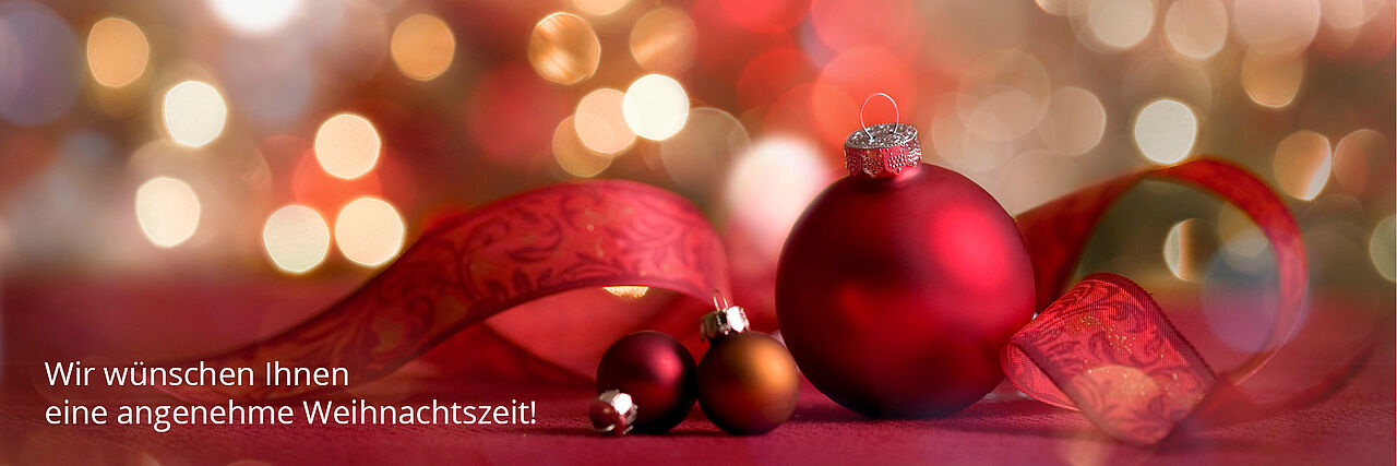Weihnachtsbaumkugeln vor einem roten Hintergrund mit Schrift "Wir wünschen Ihnen eine angenehme Weihnachtszeit"