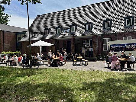 Menschen an Tischen vor einem Backsteingebäude