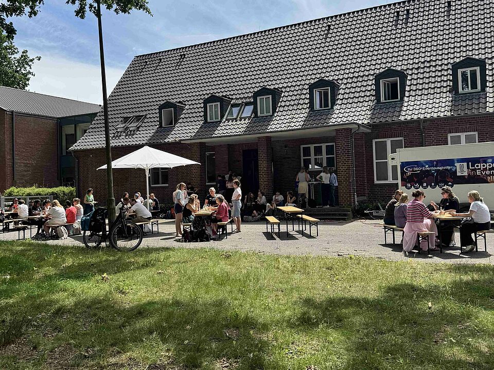 Menschen an Tischen vor einem Backsteingebäude