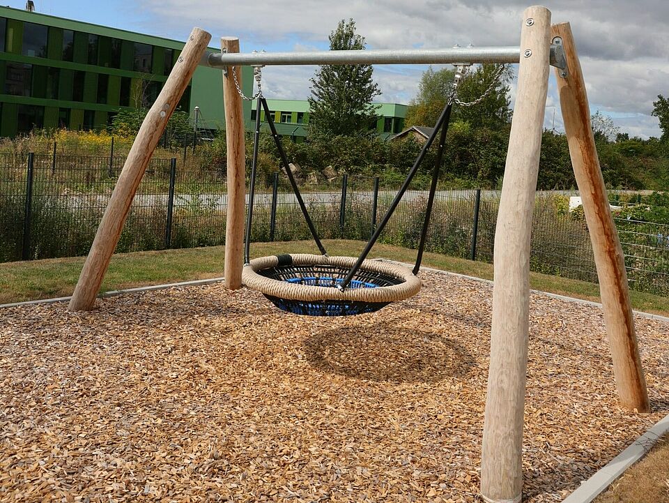 Eine blaue Korbschaukel an einem Gerüst auf einem mit Rindenmulch ausgelegtem Platz