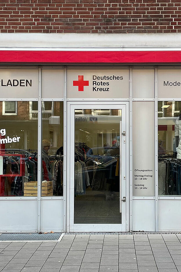 Schaufenster eines Ladenlokals mit Kleiderpuppen und einem Roten Kreuz