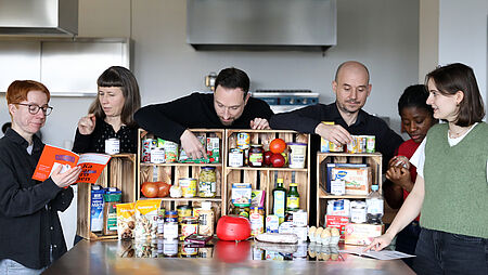 & Personen stehen hinter einem Tisch, auf dem viele konservierte und trockene Lebensmittel stehen