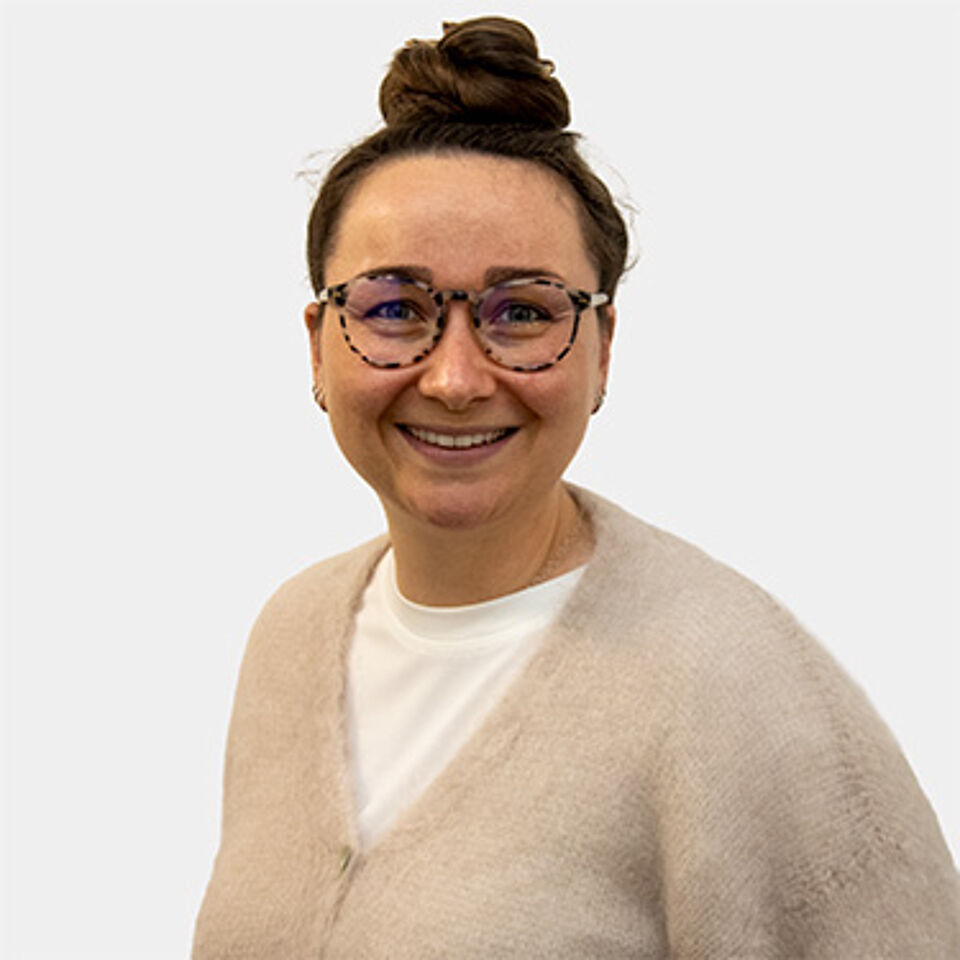 Eine junge Frau mit Brille und braunen Haaren zu einem Dutt gebunden.