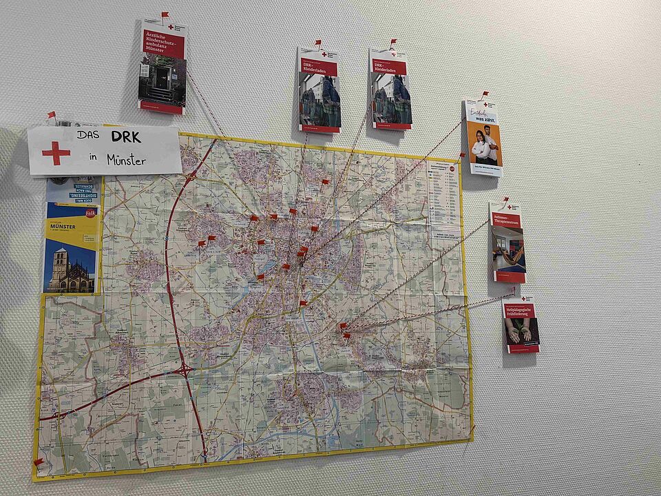 Eine Stadtkarte von Münster, auf der die DRK-Standorte eingezeichnet sind. Drumherum hängen Flyer der Einrichtungen