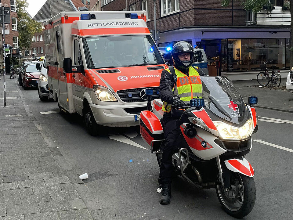 Ein Motorrad des DRK Herten mit einer Person in Einsatzkleidung, im Hintergrund ein Rettungswagen der Johanniter