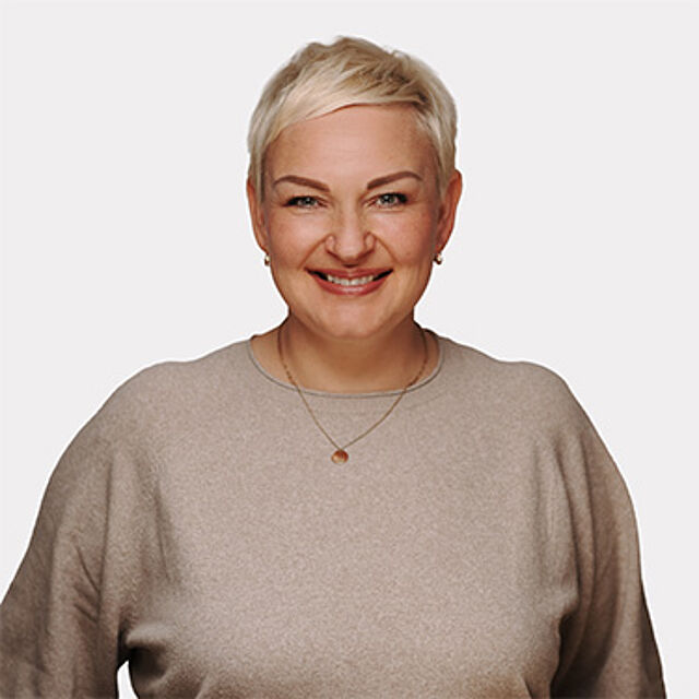Frau mit kurzen blonden Haaren, schwarzem Oberteil und braunem Blazer