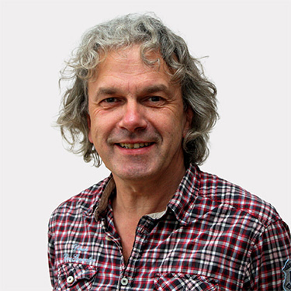 Mann mit grauen Locken und karrierten Hemd vor weißem Hintergrund