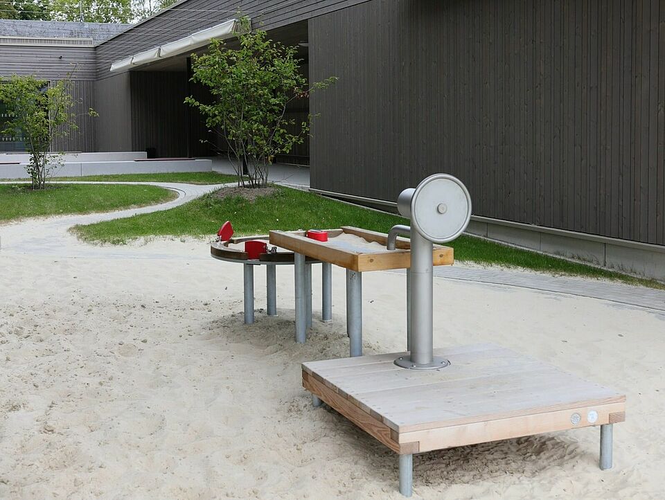 Ein Sandkasten in einem Innenhof eines modernen Gebäudes mit einem Wasserspielzeug.