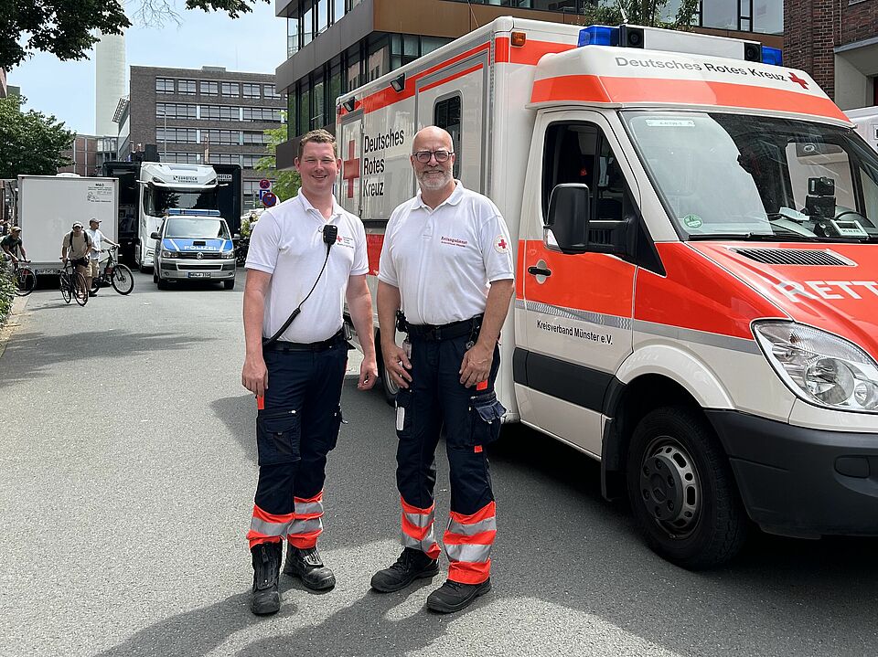 Zwei Einsatzkräfte in Einsatzkleidung stehen vor einem DRK-Krankentransportwagen