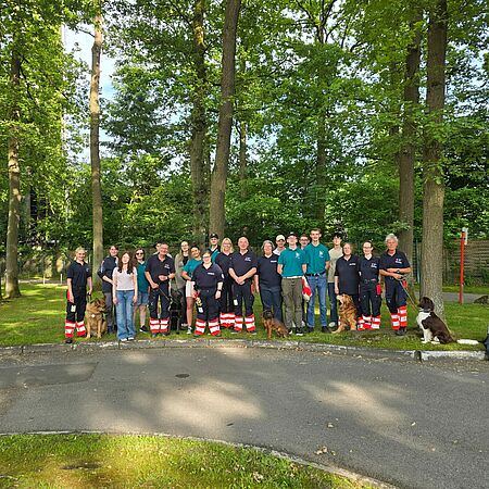 Eine Gruppe von Personen in Einsatzkleidung mit Hunden steht im Grünen.