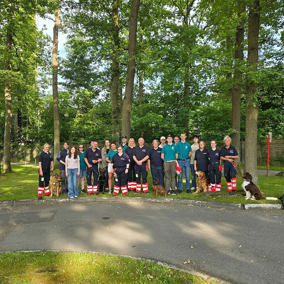 Eine Gruppe von Personen in Einsatzkleidung mit Hunden steht im Grünen.