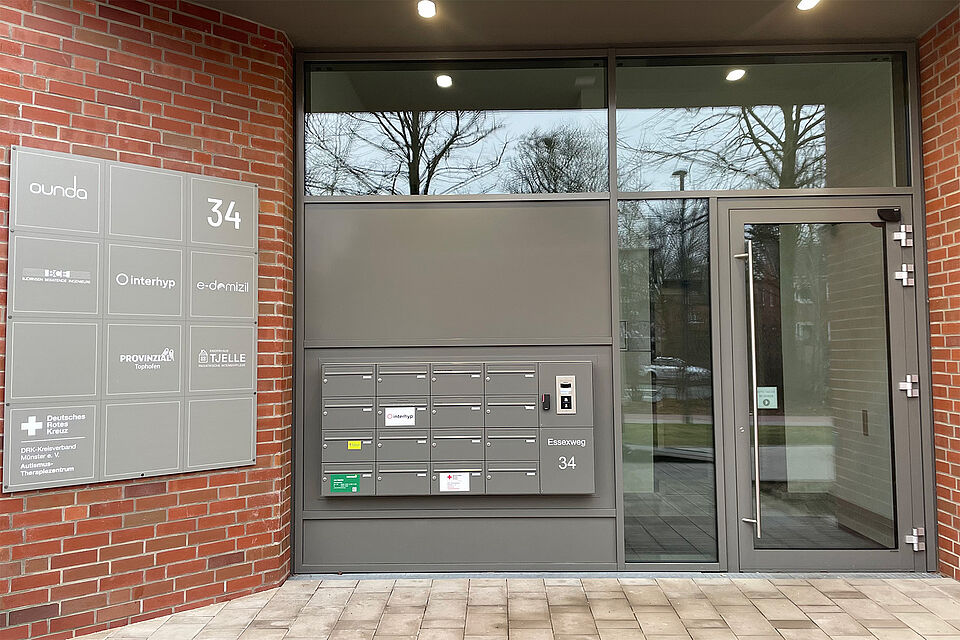 Ein breites gläsernes Portal mit dunkelgrauem Rahmen und Beschilderung.