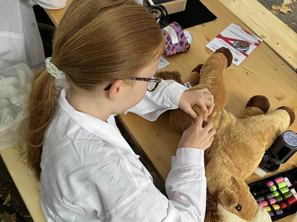 Ein Mädchen in weißem Kittel näht ein Kuscheltierpferd.