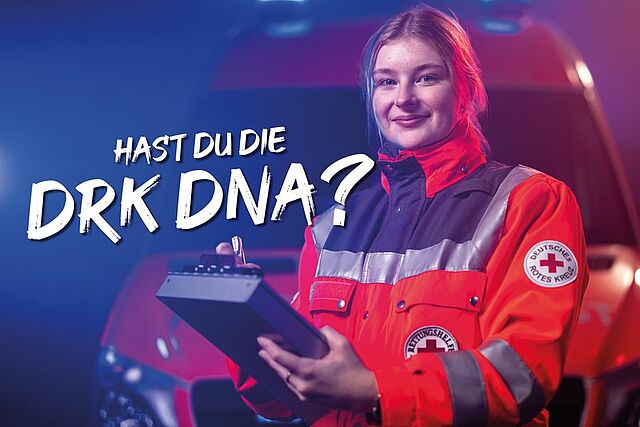 Eine Person in Einsatzkleidung mit dem Logo des Deutschen Roten Kreuzes am Ärmel hält ein Klemmbrett. Im Hintergrund steht ein Fahrzeug mit eingeschaltetem Blaulicht. Text im Bild: „Hast du die DRK DNA?“