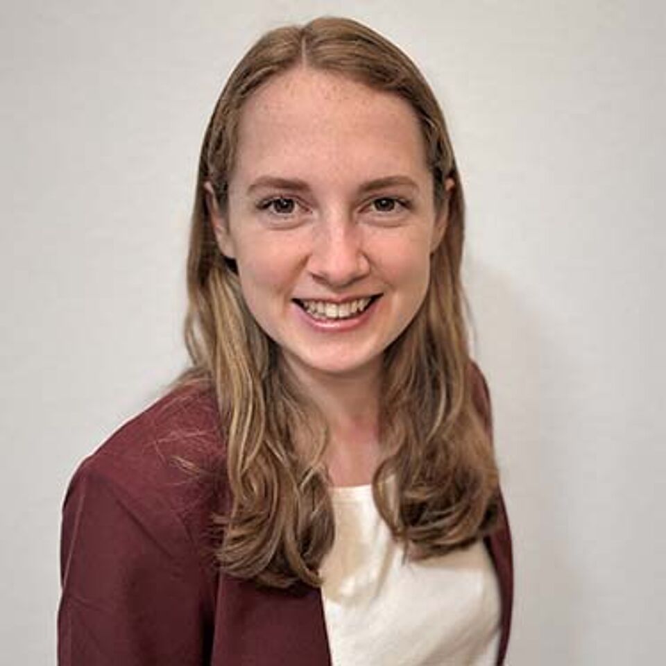 Junge Frau mit blonden Haaren, weißem Oberteil und beerenfarbenen Blazer vor weißem Hintergrund