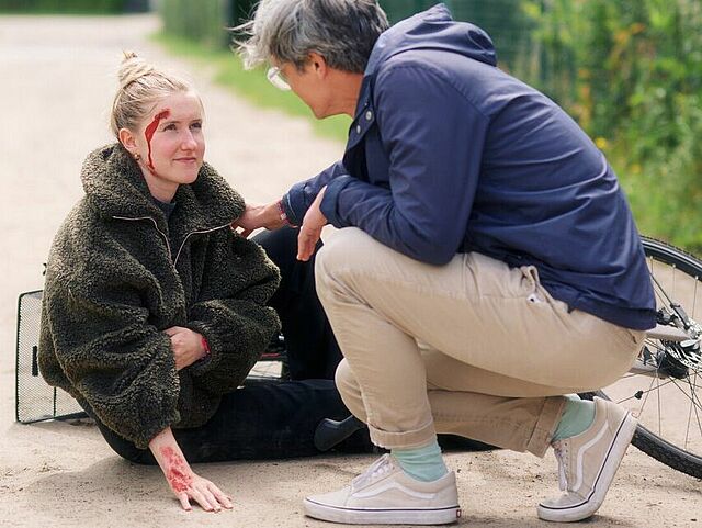 Ein Mann leistet bei einer Frau nach einem Fahrradsturz Erste Hilfe