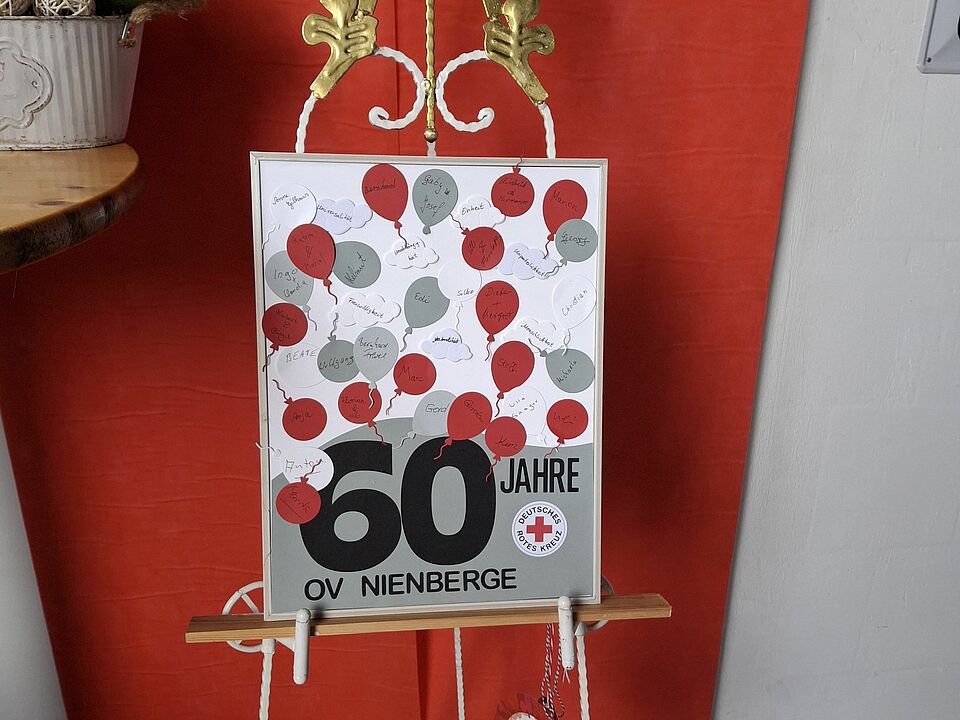 Ein Plakat auf einer Staffelei mit dem Schriftzug "60 Jahre OV Nienberge"  kleinen Luftballons, auf denen sich Unterschriften befinden.