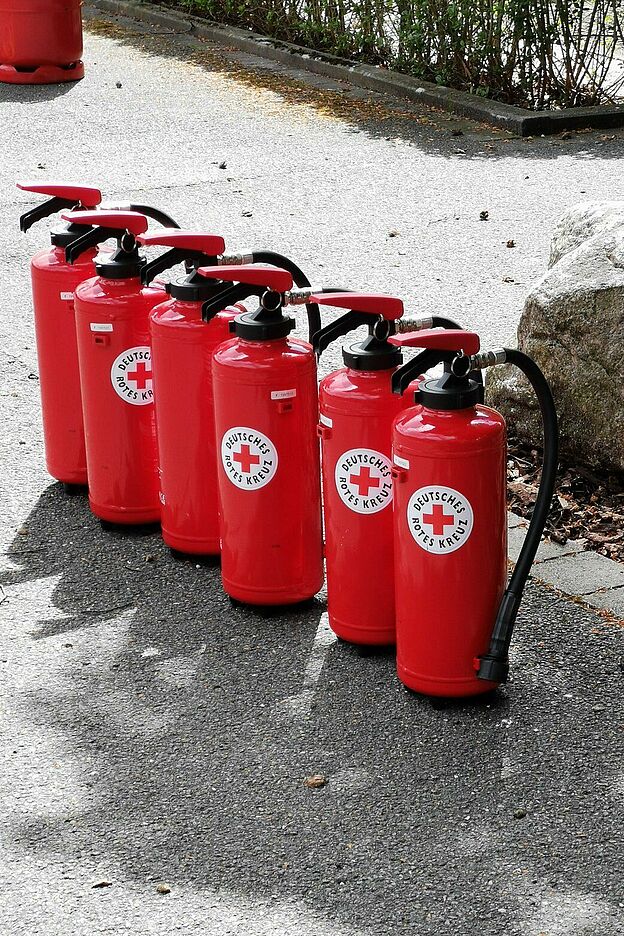 Mehrere rote Feuerlöscher mit DRK-Logo stehen in einer Reihe