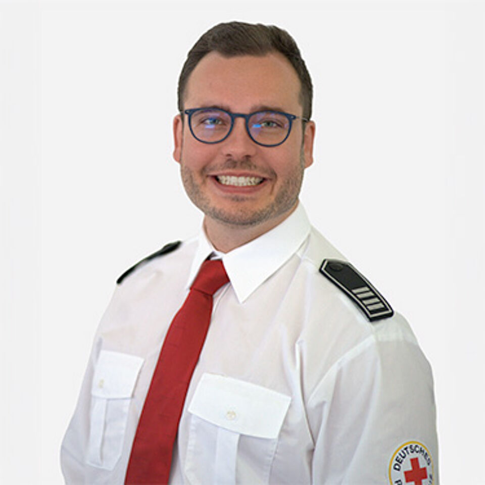 Mann in weißem Hemd und roter Krawatte mit Schulterklappen vor weißem Hintergrund