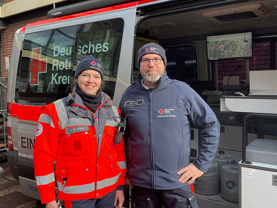 Eine Frau und ein Mann in Einsatzbekleidung des DRK stehen vor einem Einsatzleitwagen