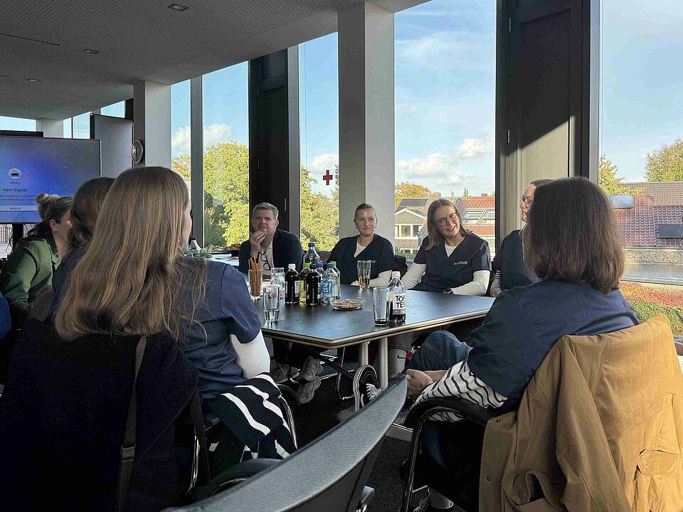 Personen sitzen an einem Tisch, auf dem Getränke und Snacks stehen, zusammen