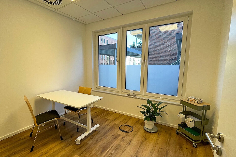 Ein Raum mit Fenster, einem eckigen Tisch und 2 Stühlen.