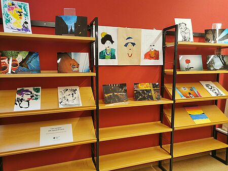 Holzregale, auf denen Bilder liegen, vor einer roten Wand