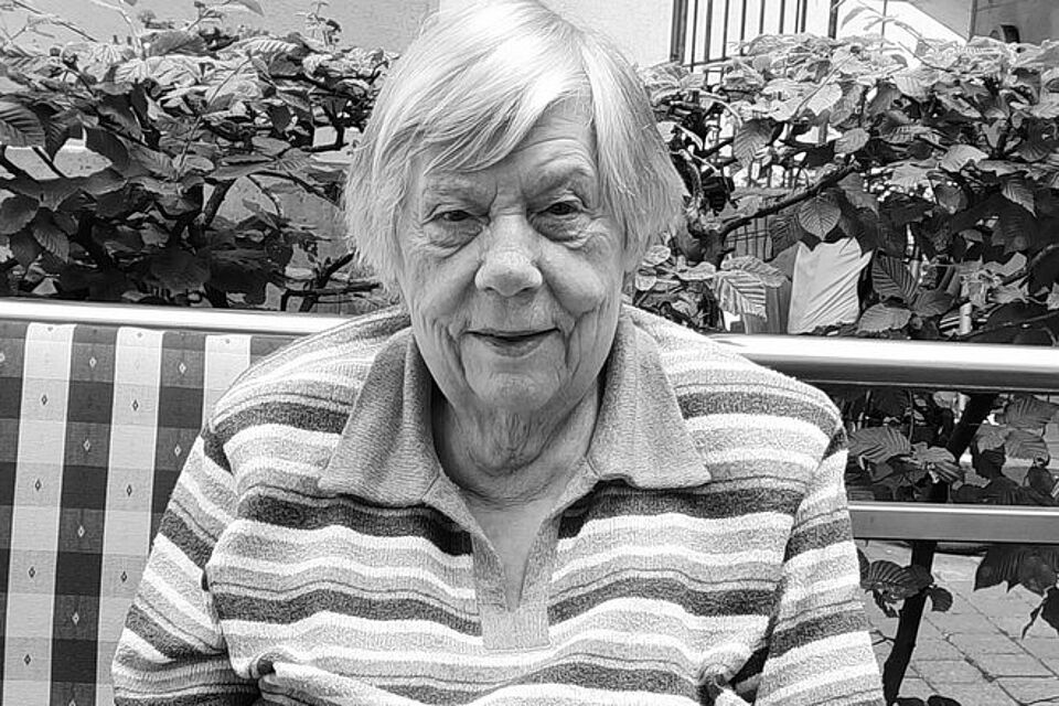 Maria Bruns Eine ältere Frau sitzt auf einer Bank, im Hintergrund eine Hecke. Das Bild ist schwarz-weiß.