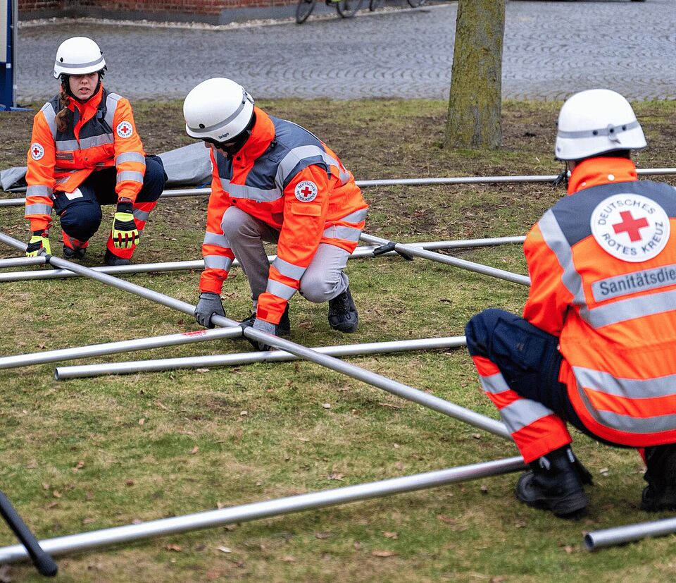 Vier Personen in Einsatzkleidung bauen ein Zelt auf