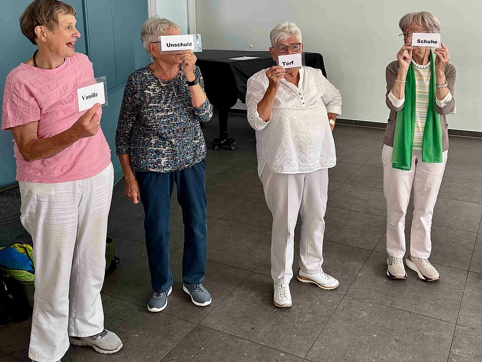 Mental und Gedächtnistraining Vier älteren Frauen stehen in einer Reihe und halten Kärtchen mit Begriffen hoch